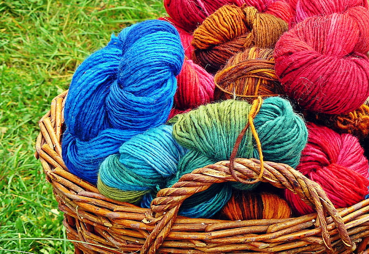 Many colorful balls of yarn for knitting. Multicolored yarn for knitting is  gathered in a heap. Knitted clothes, knitting needles and yarn in the  background of a plaid. Stock Photo