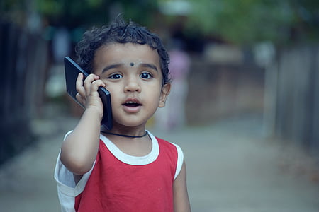 shallow focus photography of toddler in red top holding black smartphone