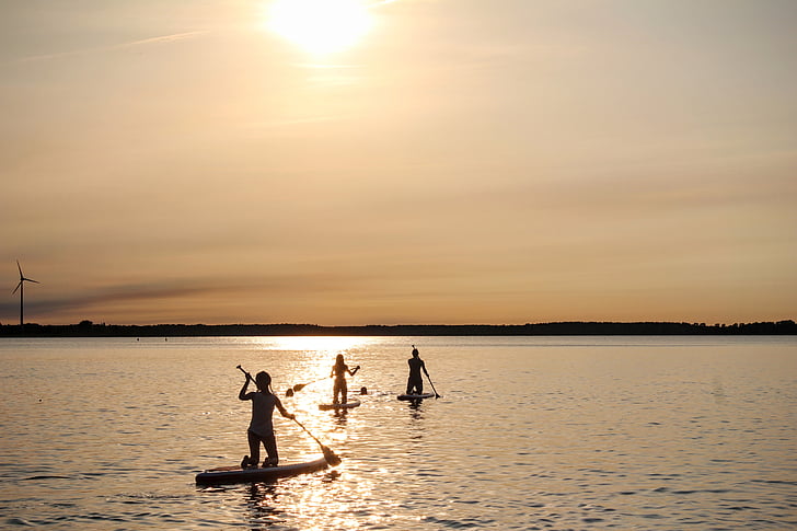 three people riding paddle board under golden hour