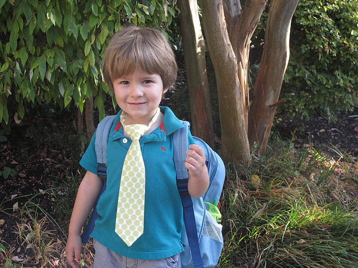 boy in blue polo shirt with backpack near tree
