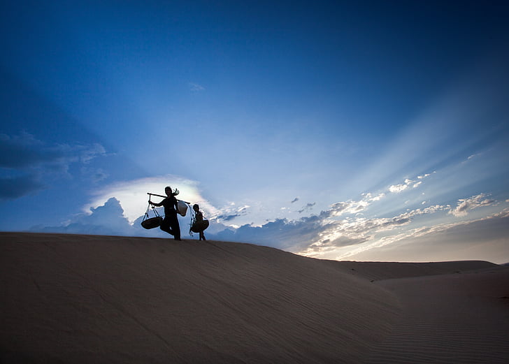 two people walking on top of sand dune under clear sky during daytime