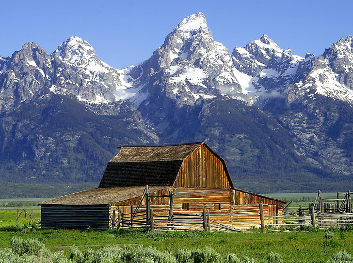 brown wooden barn near the snow capped mountains under the blue sky
