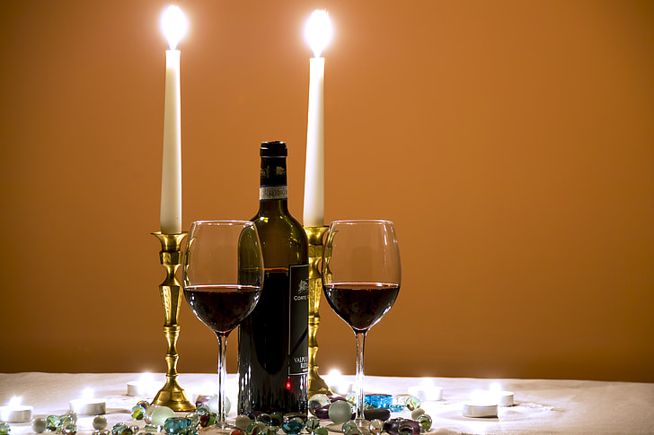 closeup photography of 3/4 full wine bottle in the middle of tall candlestick and wine glasses