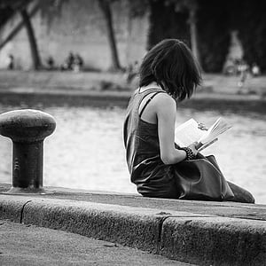 woman sitting on pavement reading book