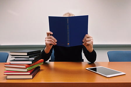 person holding blue book leaning on brown wooden desk