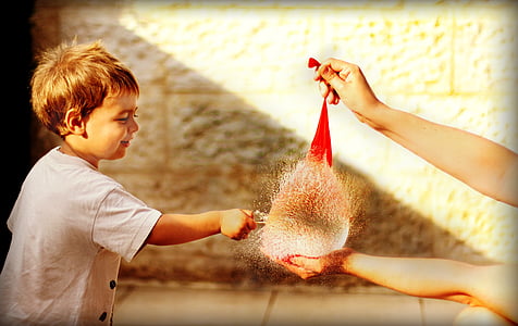 boy wearing white shirt popping a red water balloon