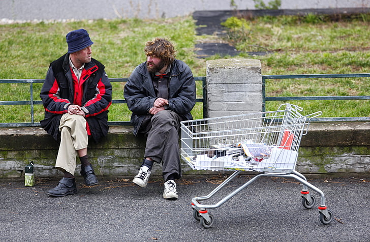 two men sitting on bench near white shopping cart