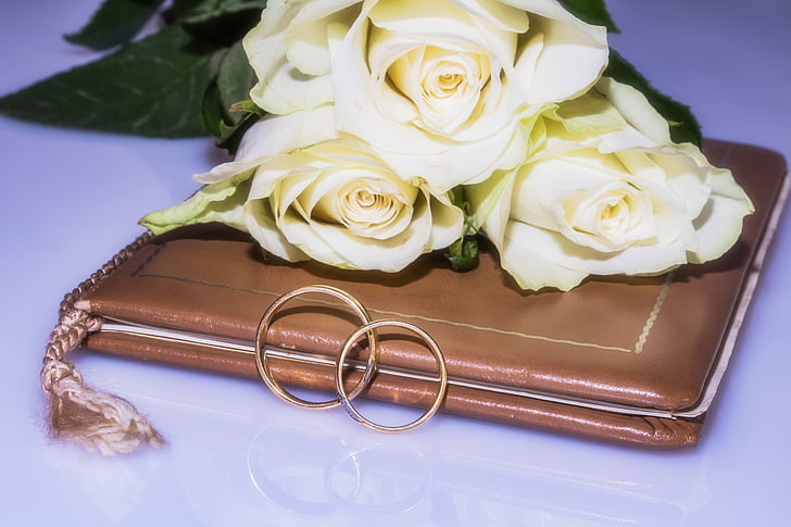 two gold-colored couple ring on book with bouquet