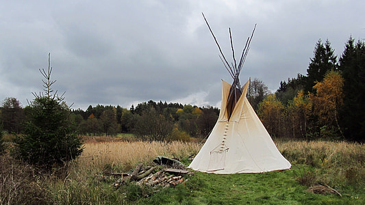 white teepee tent on green field surrounded by trees at daytime