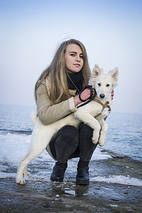 woman with white German shepherd near calm body of water at daytime