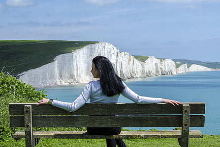 woman in white sweatshirt sitting on wooden bench near cliff during daytime