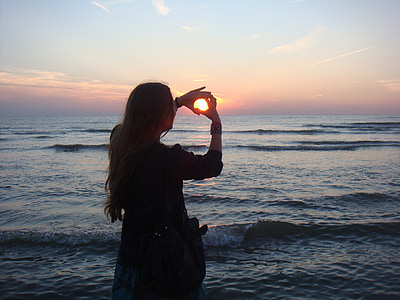 woman with black shirt hand forming hearts by the seashore