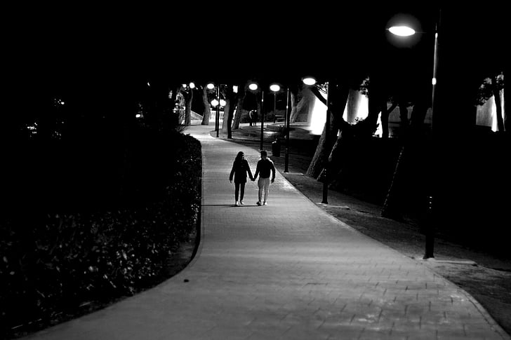 grayscale photo of male and female holding hands under light posts