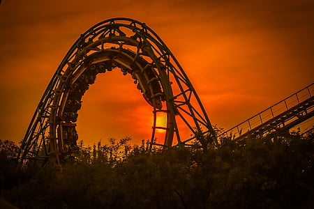 silhouette photography of round roller coaster rail with roller coaster during golden hour
