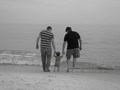 grayscale photo of two men guiding a child to walk on seashore
