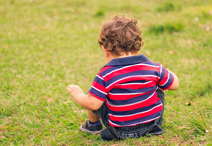 boy sitting on green grass at daytime