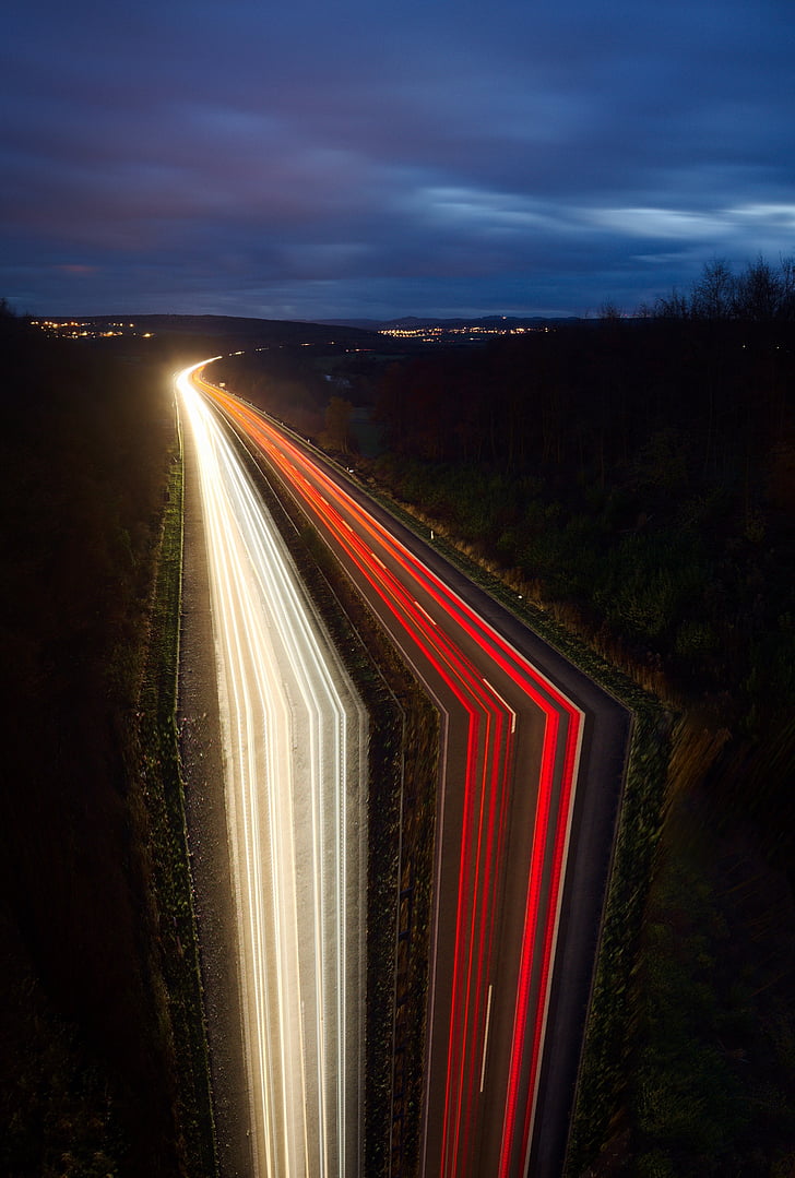 time-lapse photography of highway surrounded by trees under cloudy skies